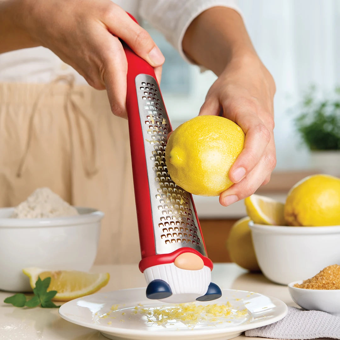 Using a red OTOTO Pepito grater, someone zesting a lemon adds flavor dust onto the kitchen counter.