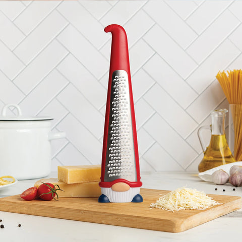 OTOTOs Pepito, a gnome-shaped cheese grater, sits near cheese, tomatoes, and spaghetti on the counter.
