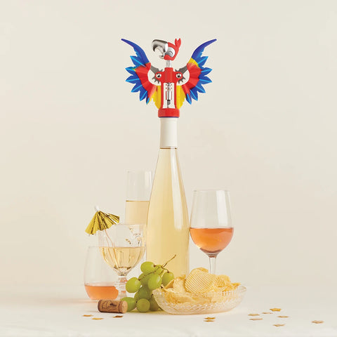 The colorful Pinot parrot wine opener perches on a bottle amid grapes, chips, and party essentials.