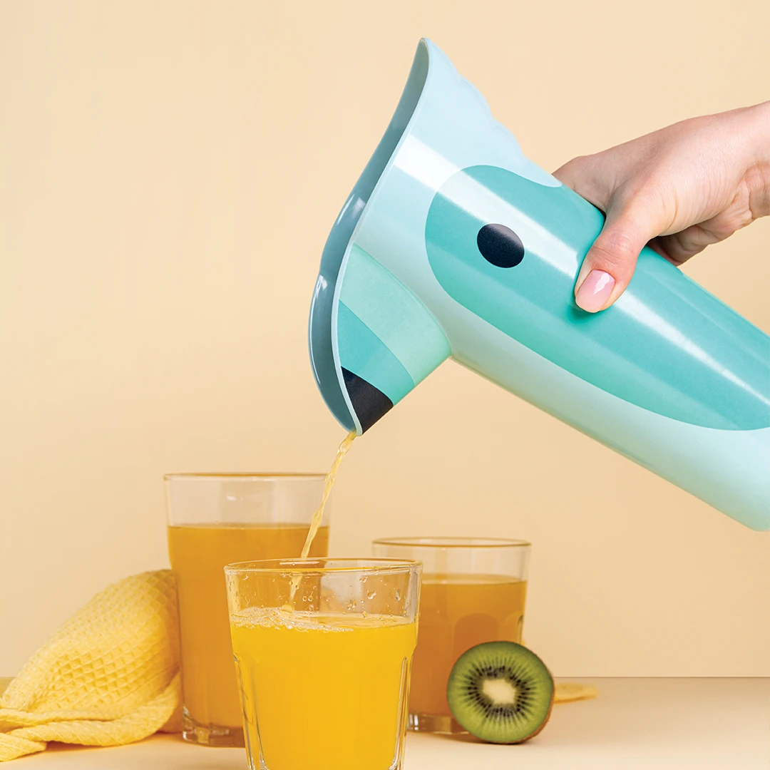 Hand pouring juice from turquoise pitcher into glass, kiwi slice nearby, against beige background.