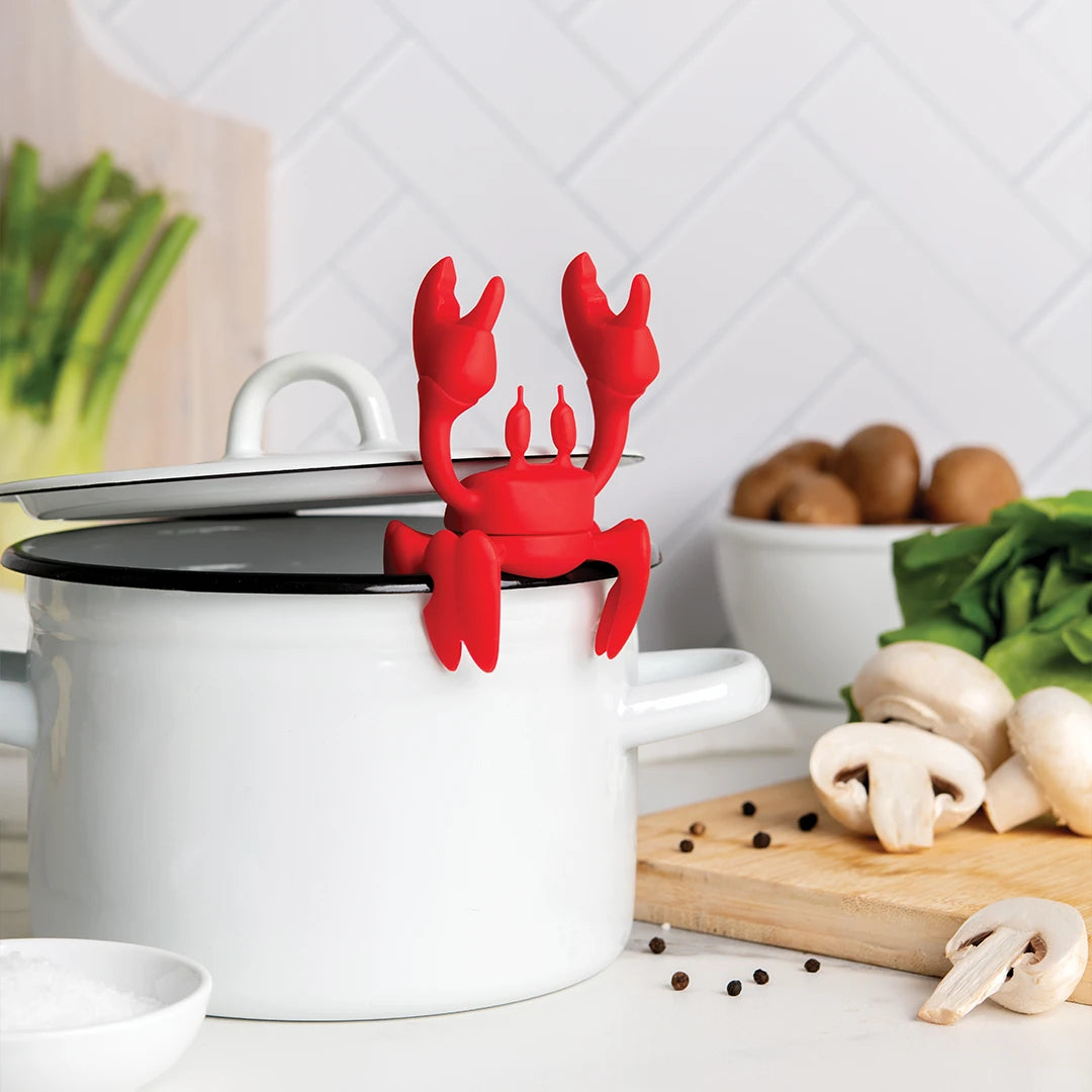 Red OTOTO utensil holder sits on a white pot, surrounded by vegetables on a cutting board.