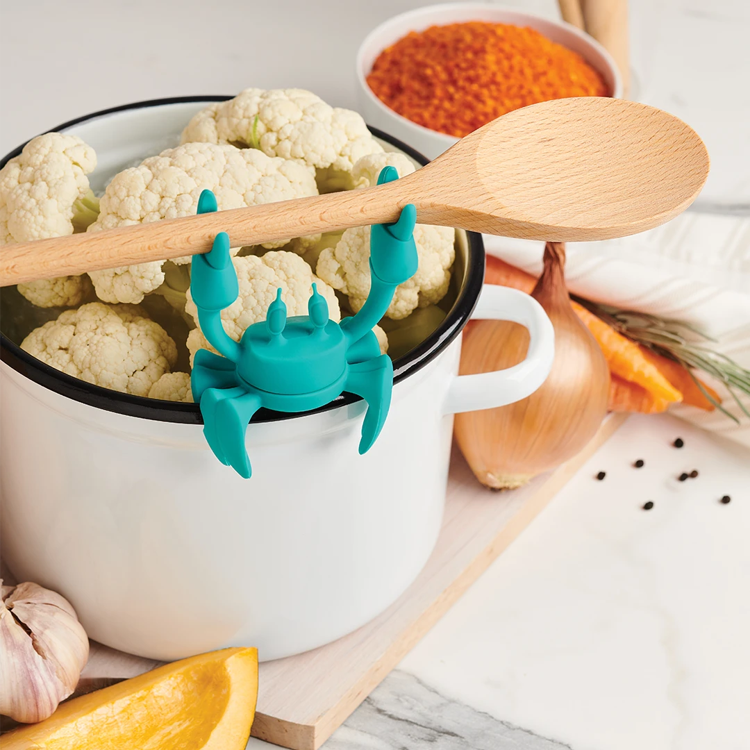 OTOTOs Aqua, a teal crab-shaped utensil rest by Dor Carmon, sits as a spoon holder on cauliflower.