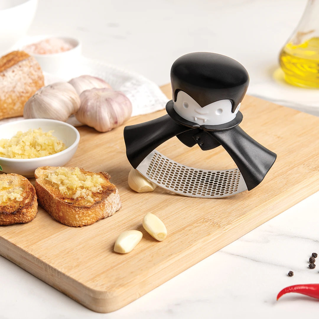Rockula garlic crusher with cloves and bread on a board, featuring a vampire theme.