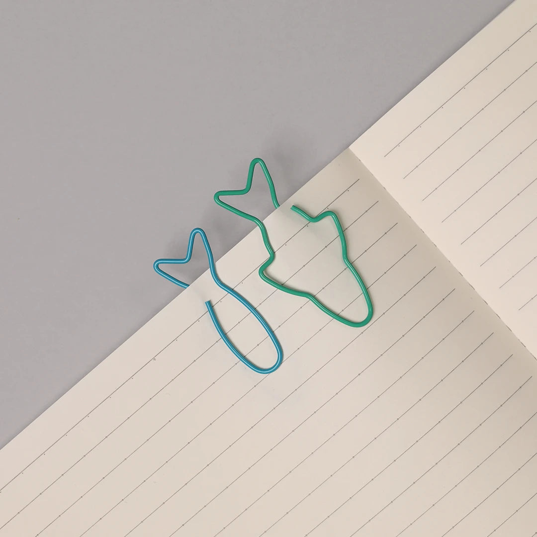 Two fish-shaped paperclips on an open notebook with lined pages, placed on a gray surface.