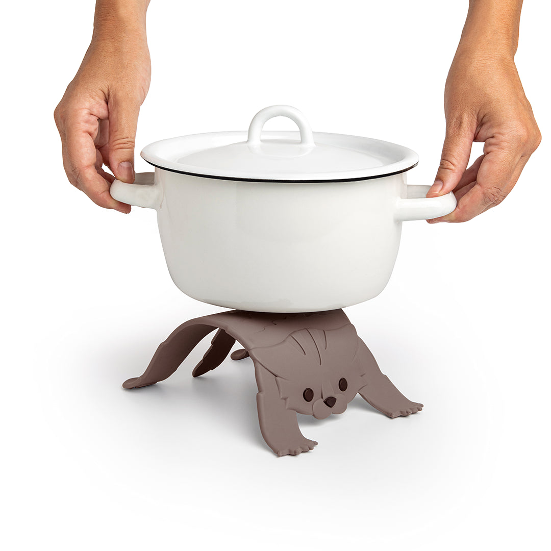 An OTOTO pot on a Scaredy Cat trivet with someone holding the hot handles.