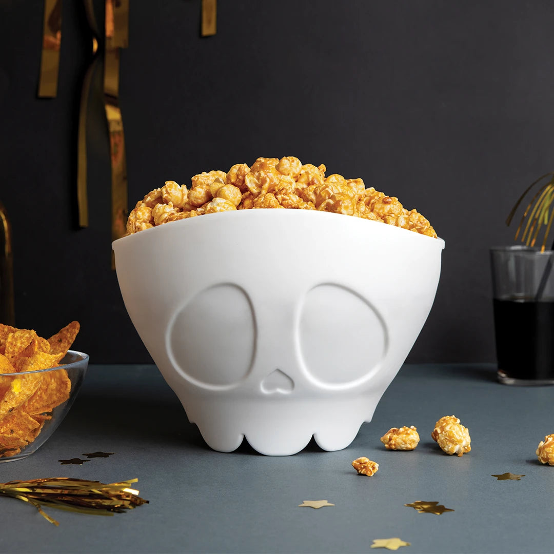 White skull bowl with Scary Poppings, snacks, a drink, and festive decor.