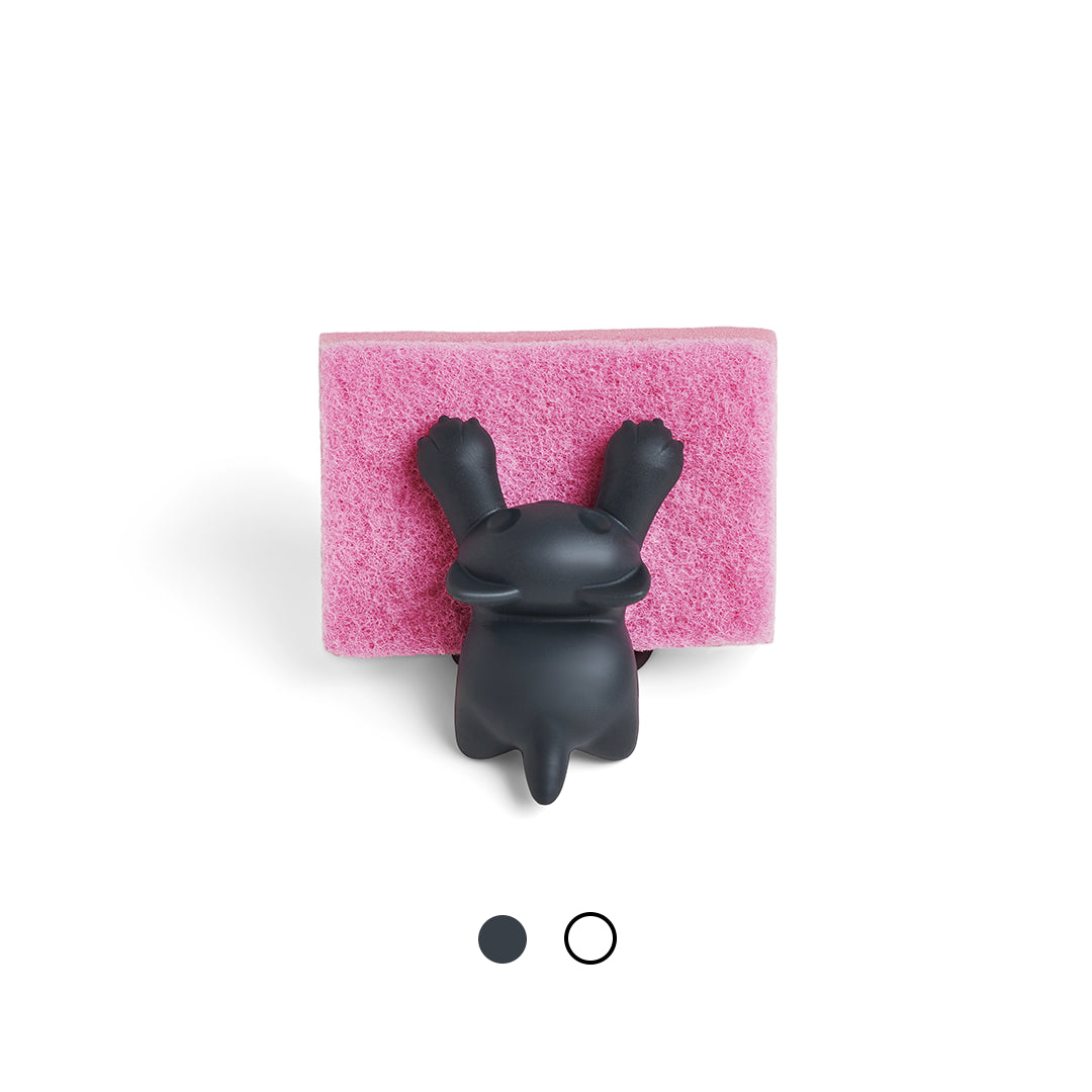 A black bunny rests on a pink OTOTO Scrubby sponge, viewed from above.