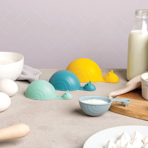 OTOTOs Shelly, a snail-shaped measuring cup set in pastel colors, amid baking ingredients in the kitchen.