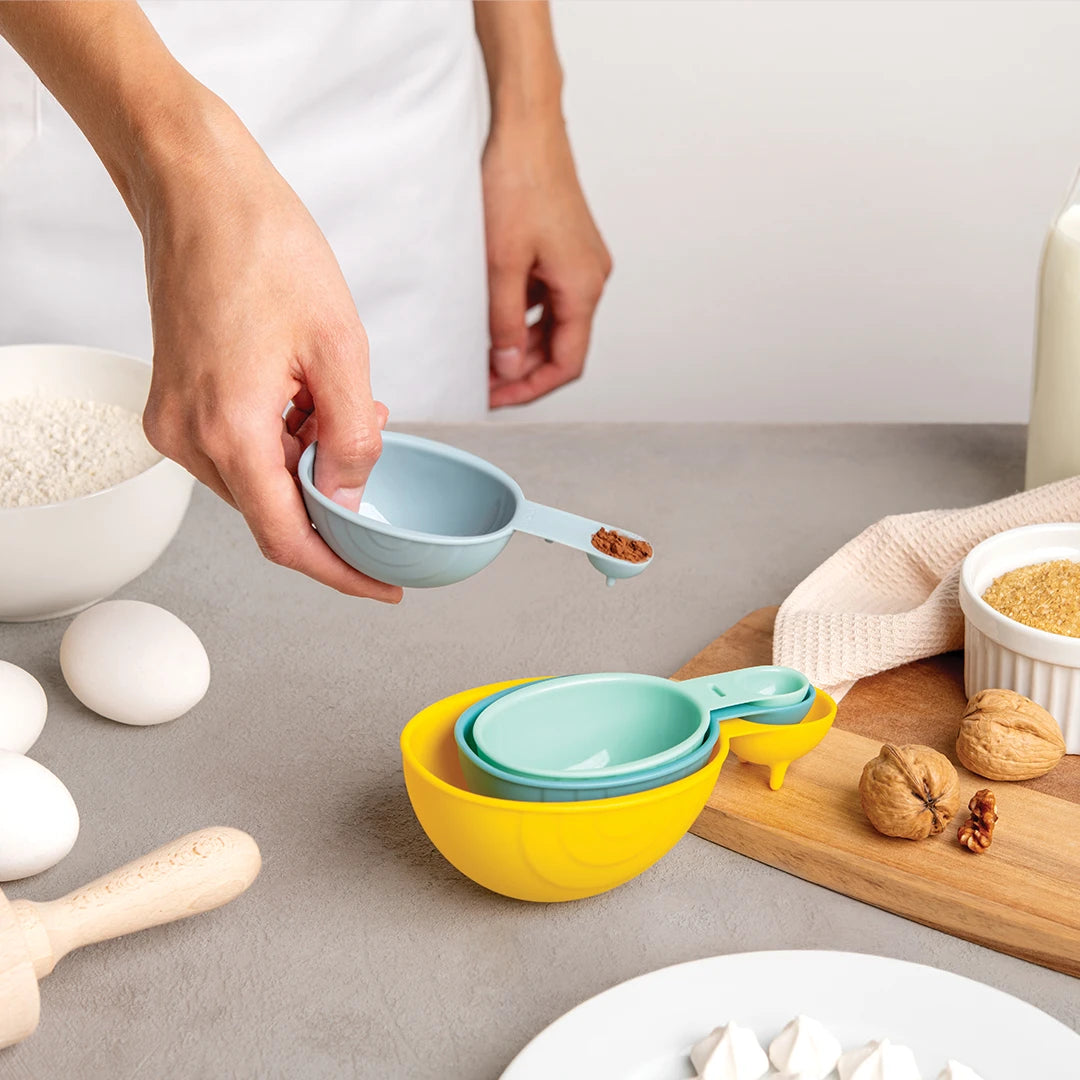 Person holding a Shelly snail-shaped measuring cup above a set of nested cups on the counter.