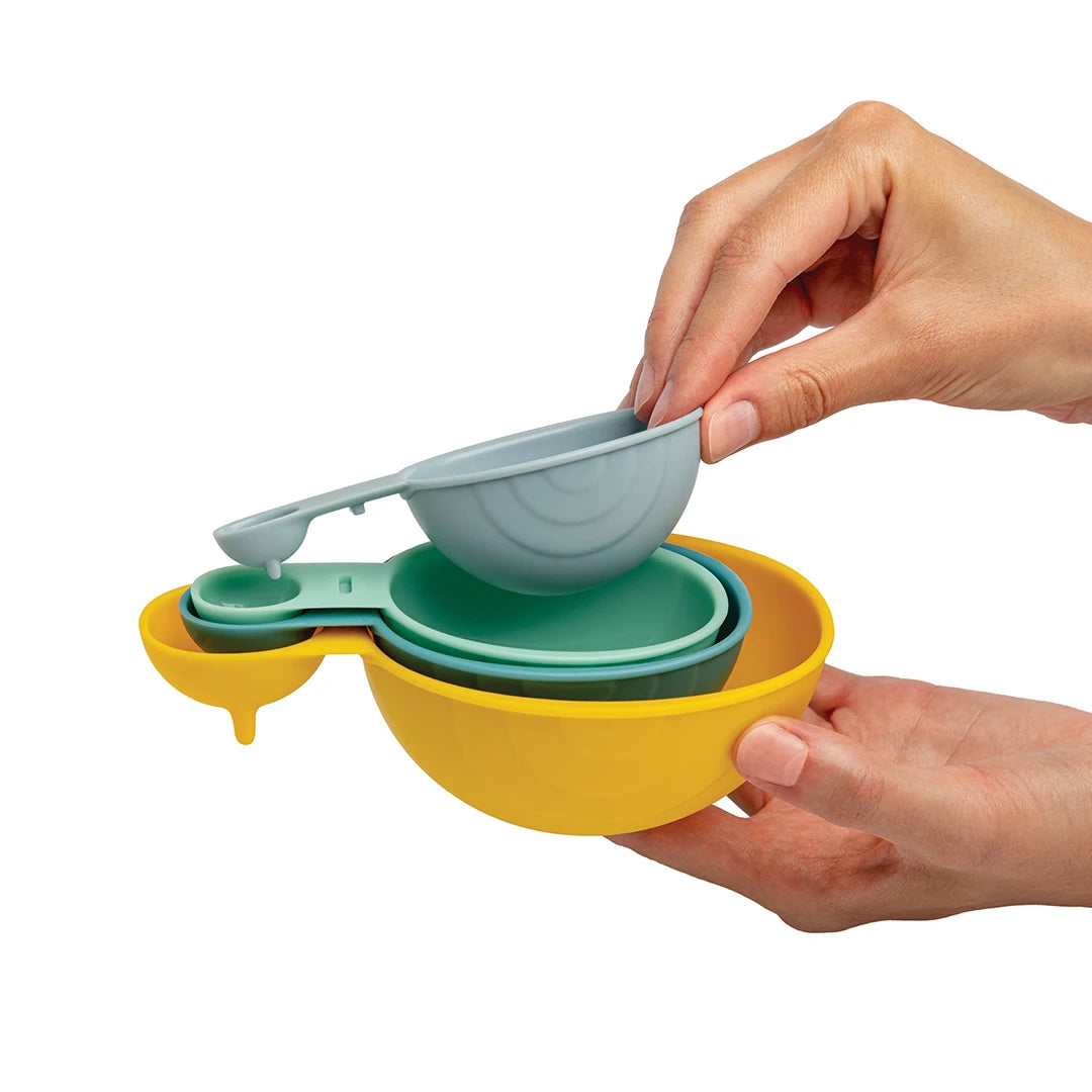 Hands holding colorful OTOTO Shelly nesting measuring cups and a snail-shaped measuring spoon set.
