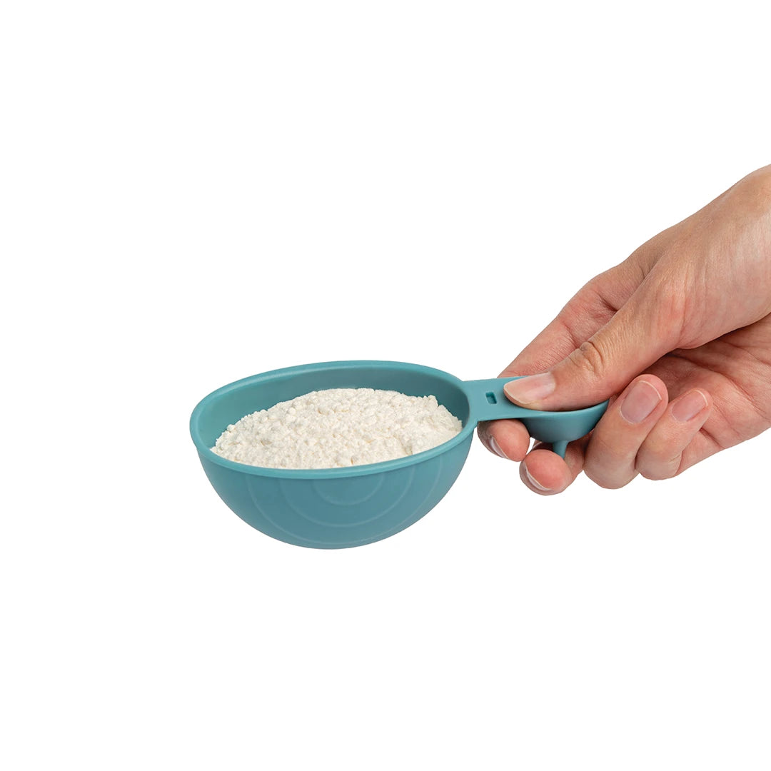 Hand holding a Shelly snail-shaped measuring cup filled with flour against a white background.