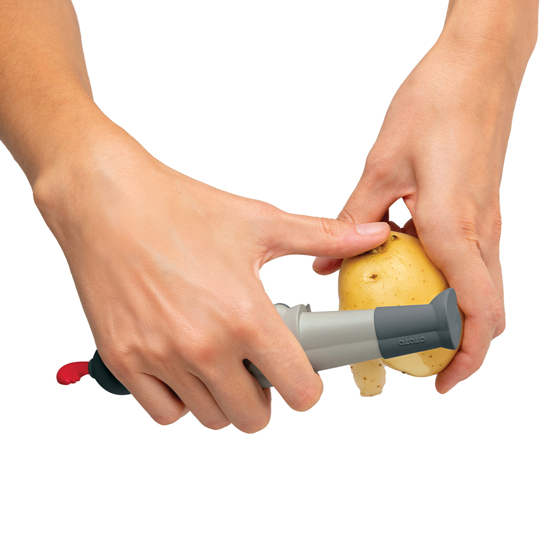 Hands expertly peeling a potato with the Sir Peels A-lot peeler against a white background.