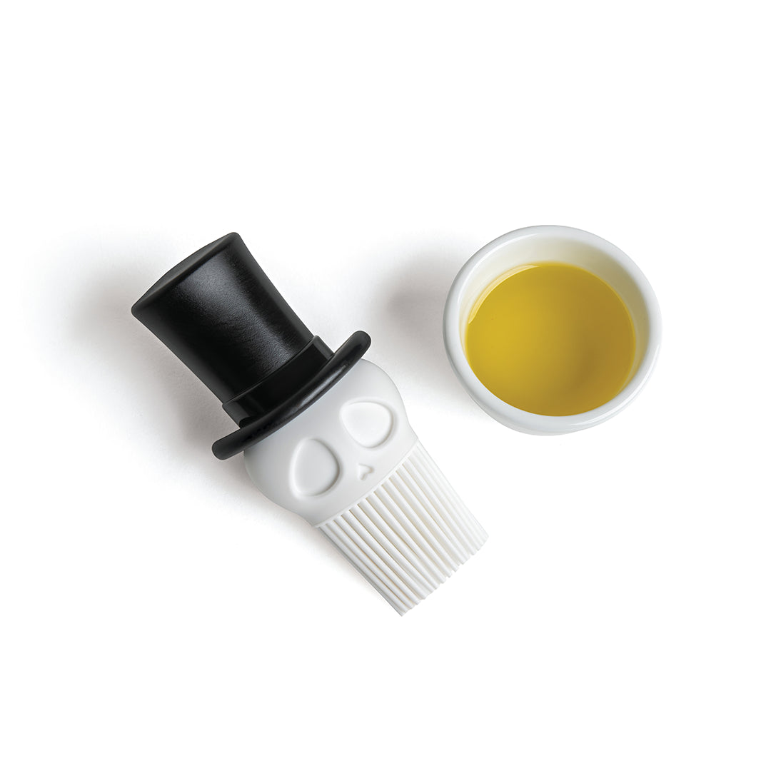 A Skully basting brush in a top hat sits by a bowl of yellow liquid, ready for cooking adventures.