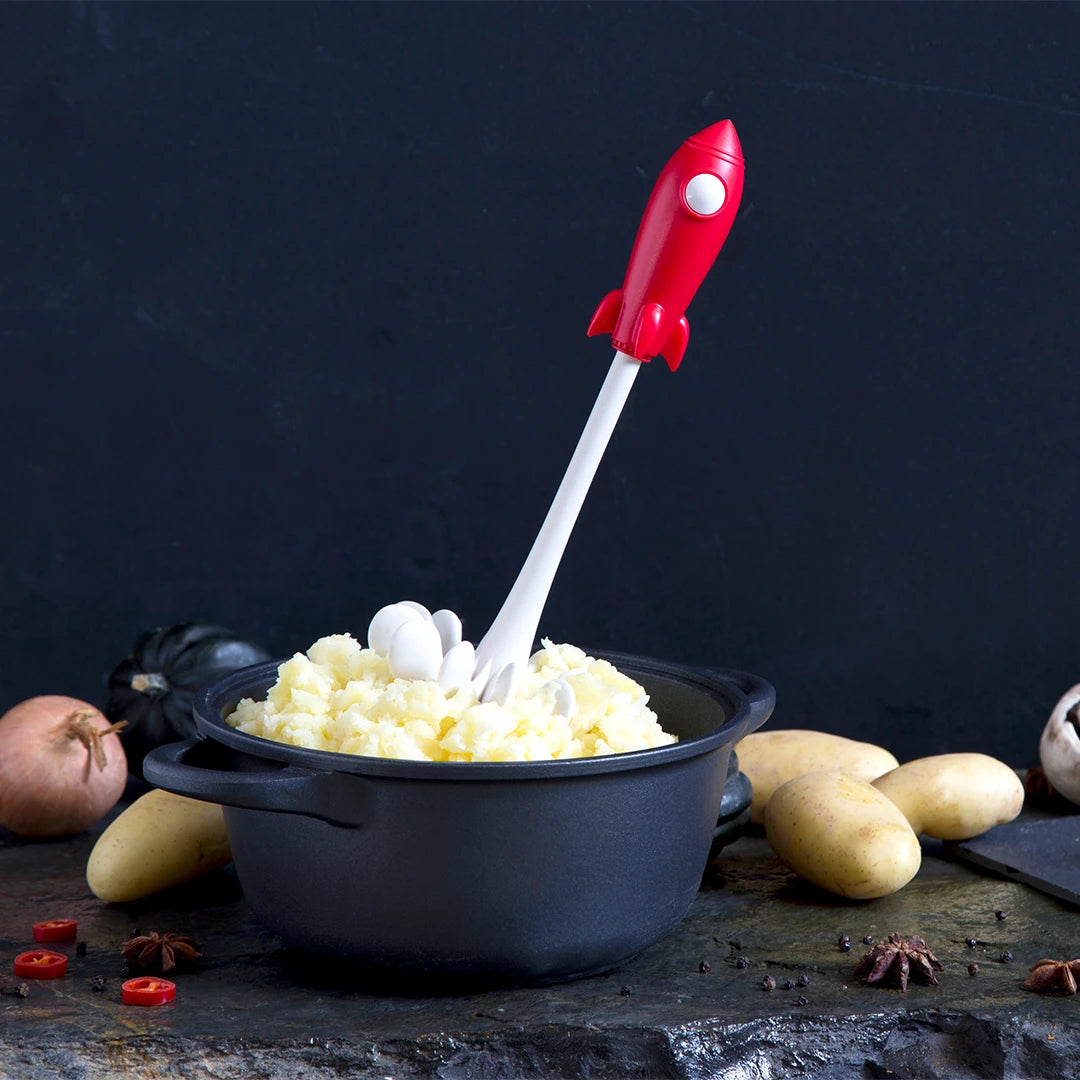 The OTOTO Space Masher, a rocket-shaped gadget, soars in mashed potatoes among spuds and onions.