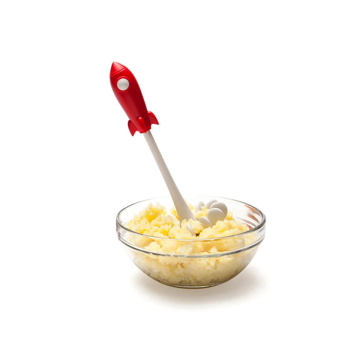 A glass bowl of mashed potatoes with a red rocket-shaped masher.
