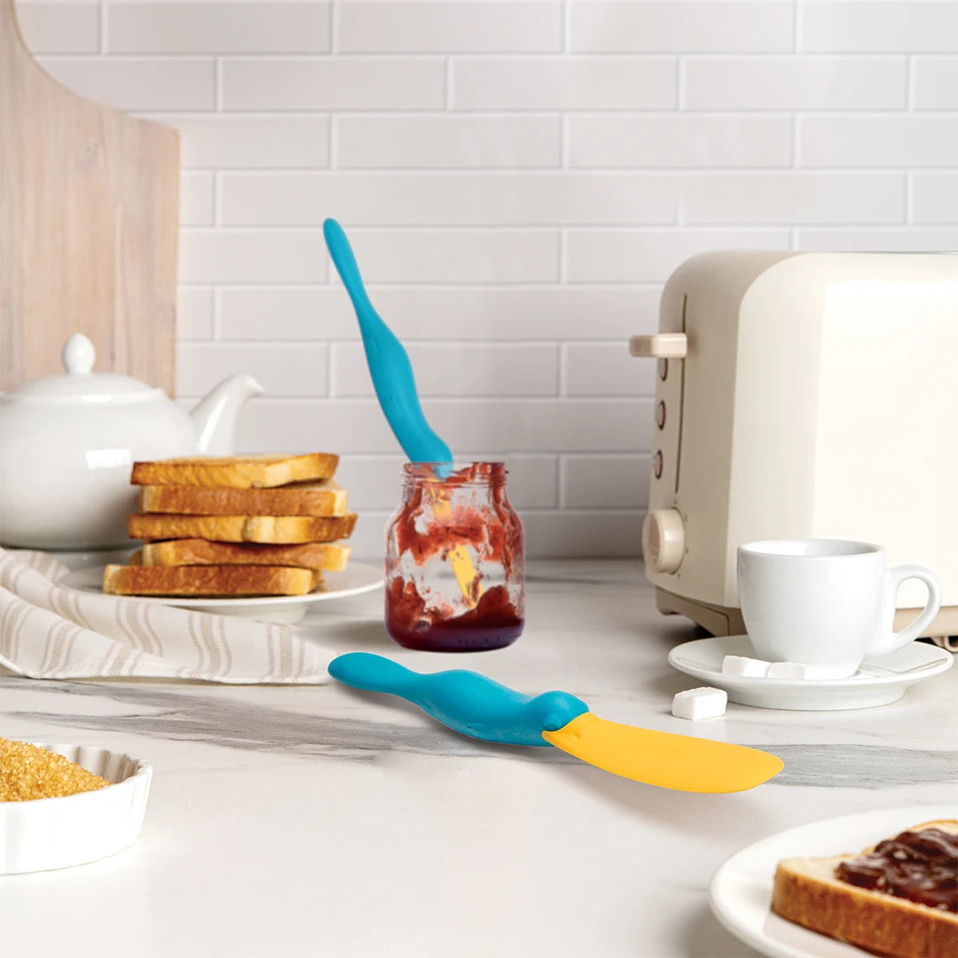 Splatypus spreaders on kitchen counter with toast, jelly jar, toaster, and tea set.