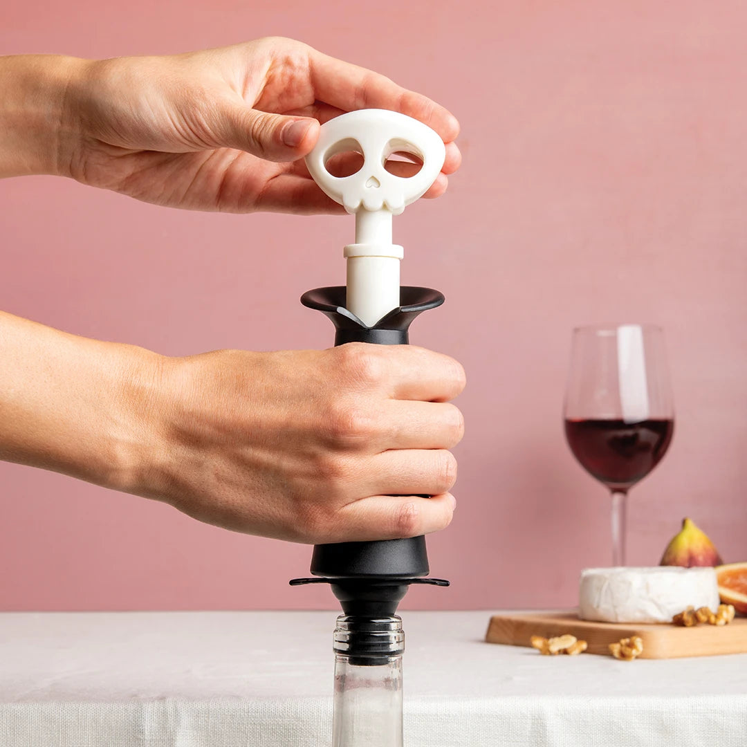 Hands using a Spookelier wine stopper, with red wine and cheese in a spooky background.
