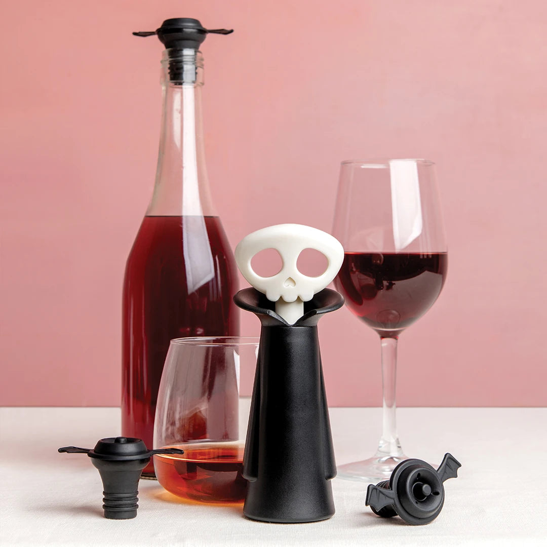 Spookelier wine set with skull stopper, glasses, bat corks on pink background.
