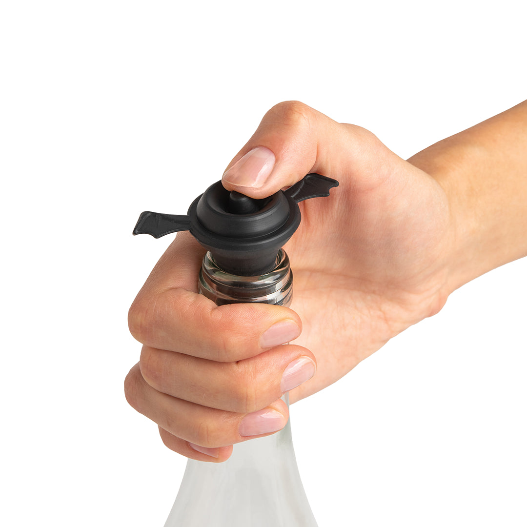 Hand holding Spookelier, a wine stopper with black winged bottle top.