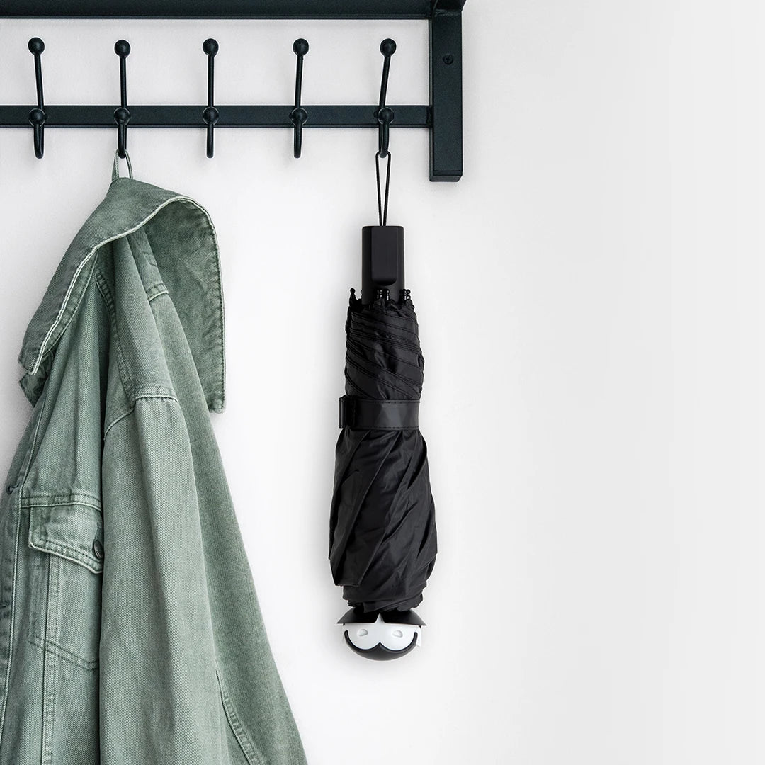 A green jacket and a stylish umbrella hang on the Spookula, a black hook rack, against a white wall.