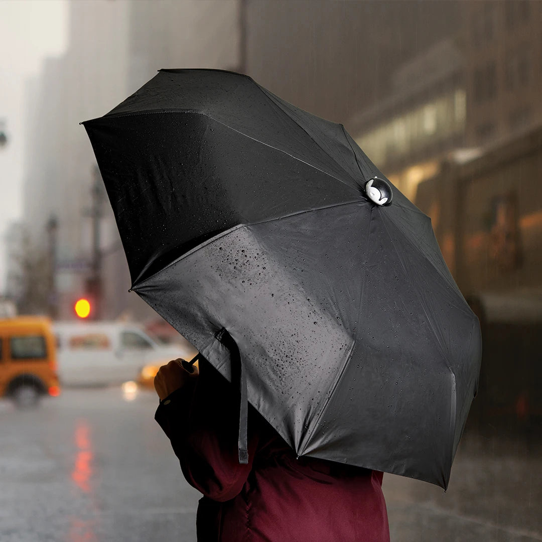 A person with a Spookula umbrella on a rainy city street, blurred buildings and cars in the backdrop.