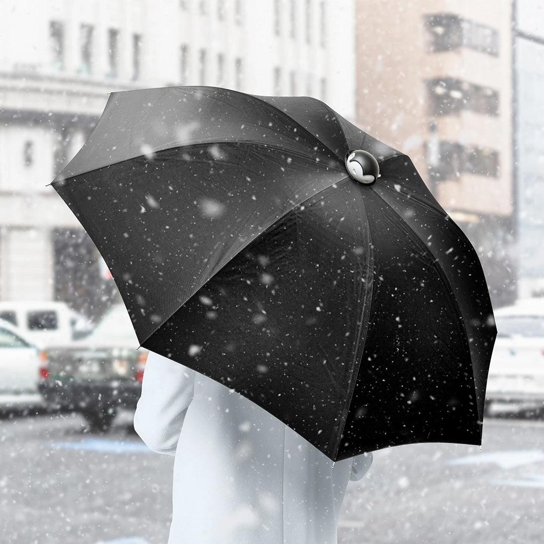 Person in coat holding black umbrella in snowy urban street with cars and buildings in the background.