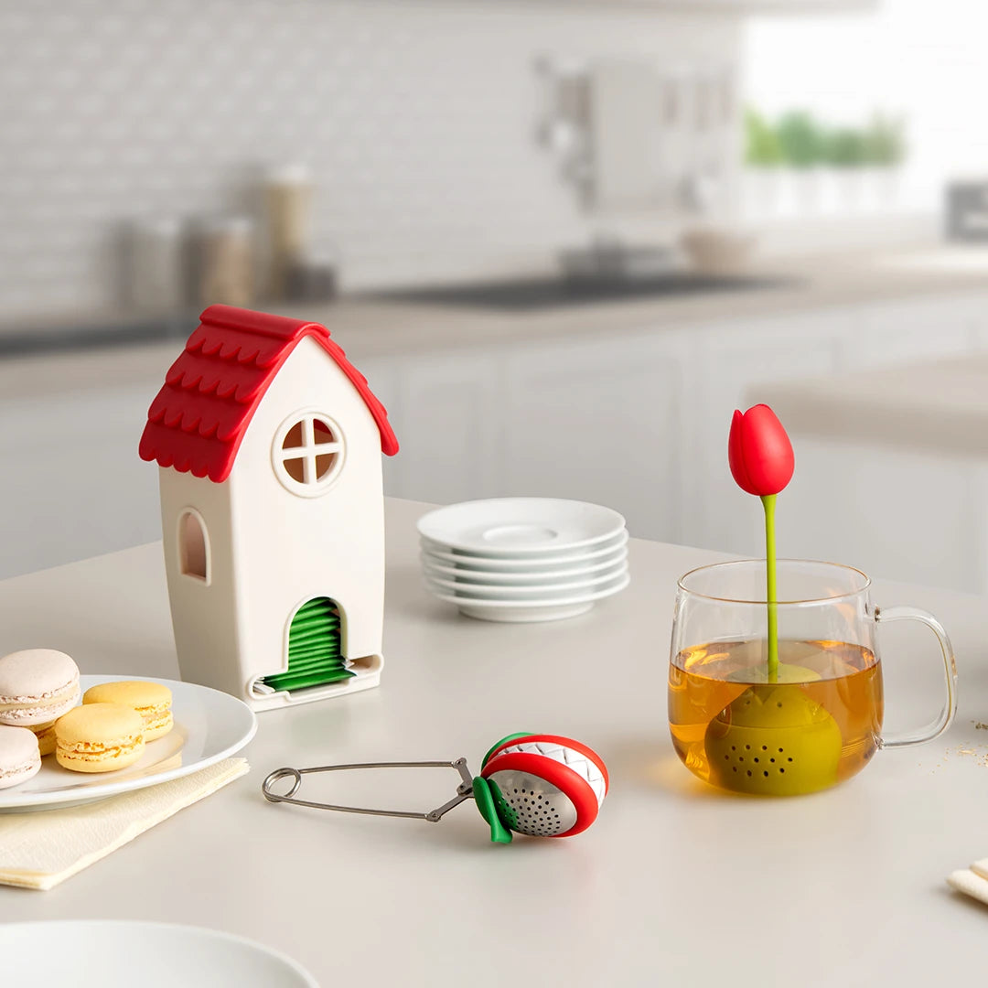 Tea Trap infusers shaped like plants and a house beside macarons and a teacup.