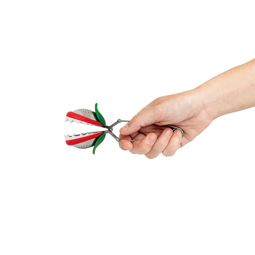 A hand holds a Tea Trap infuser, a quirky creature brimming with vibrant colors.