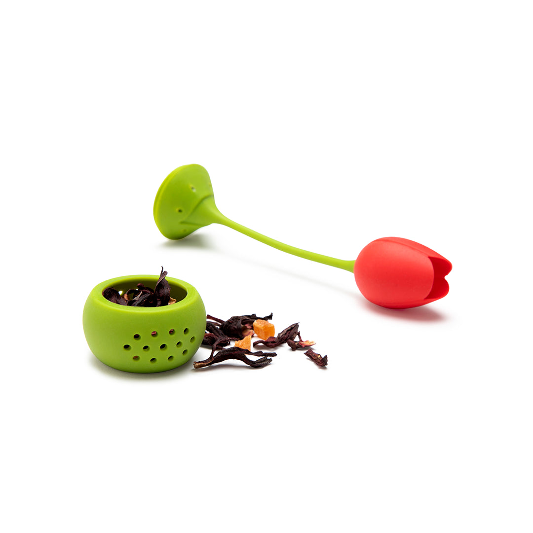 Tulip tea infuser with scattered tea leaves on a white background.