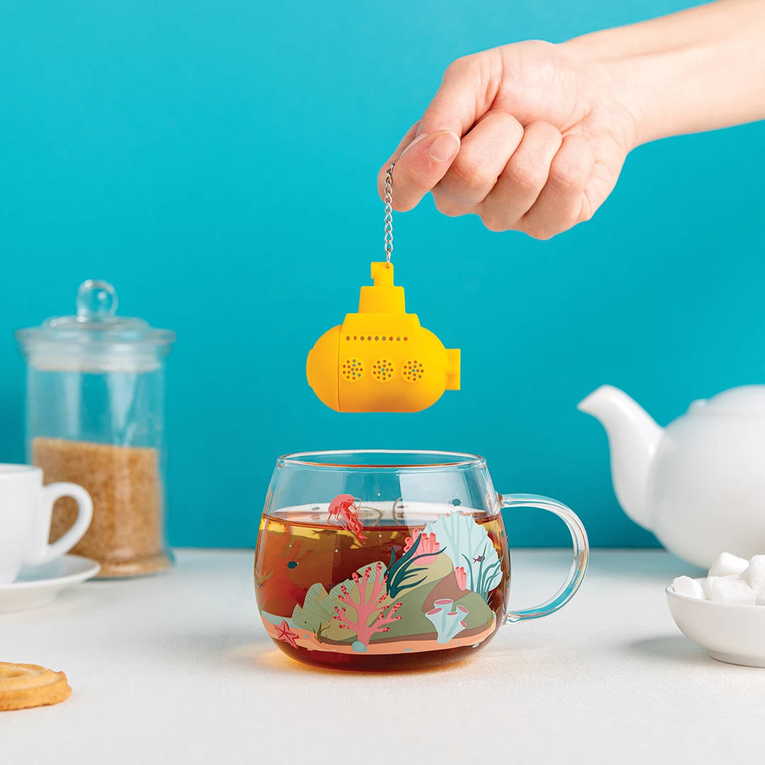 Hand displays the Under the Tea infuser, a yellow submarine held above a teacup against a blue background.
