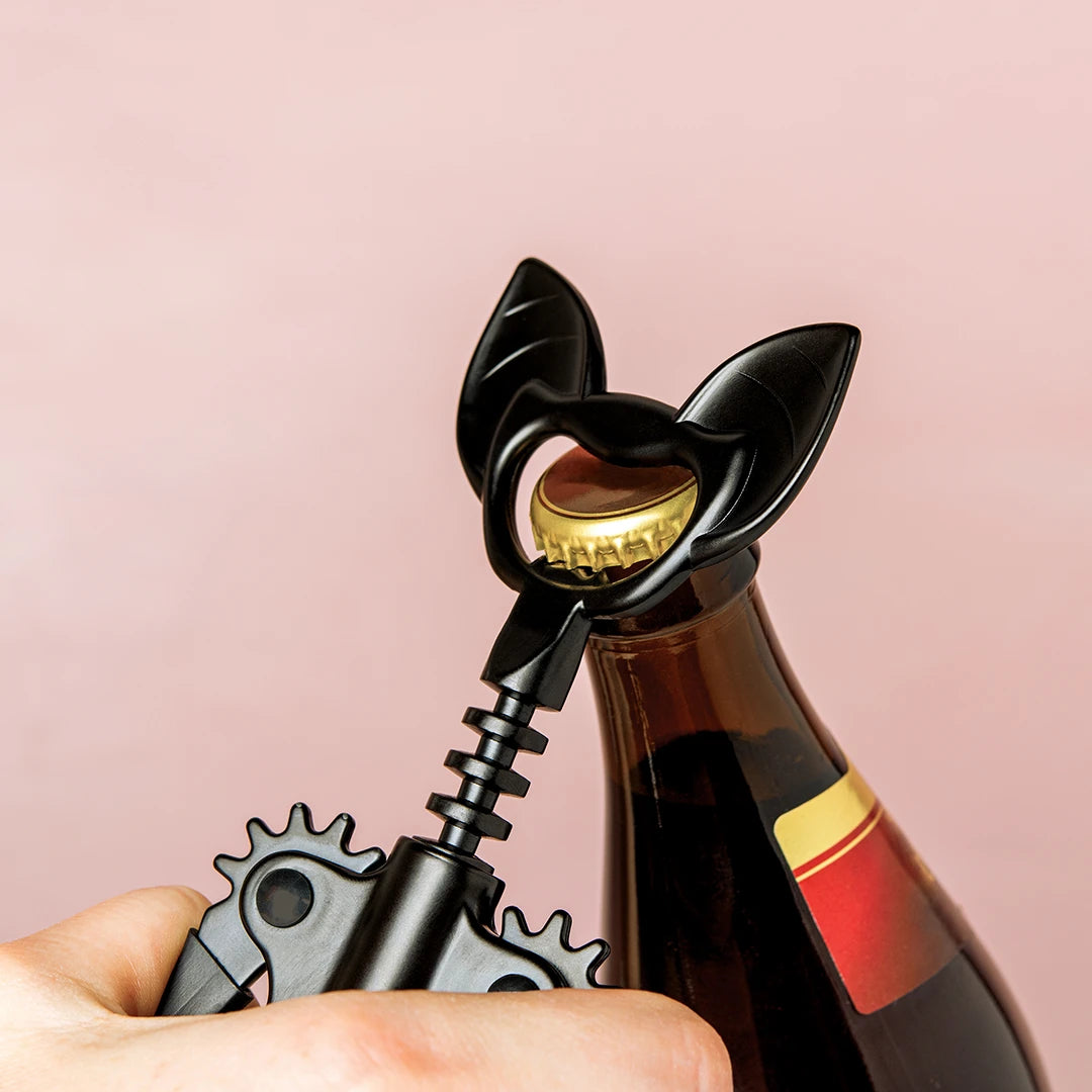 Bat-shaped corkscrew opening a bottle against a light pink background.