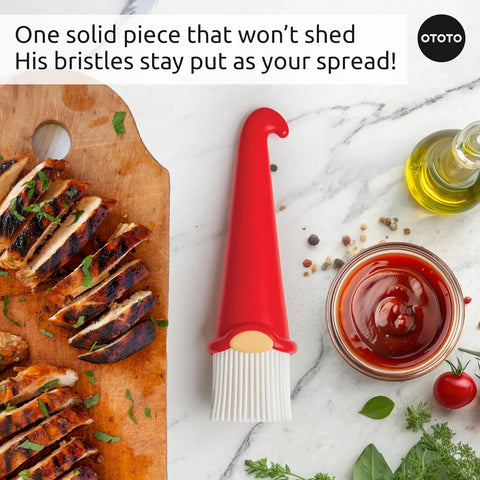 A red OTOTO Gnomeo pastry brush with sliced grilled chicken on a wooden board, herbs, oil, and sauce.