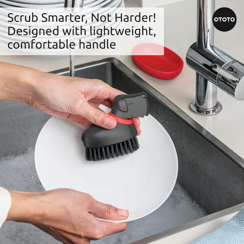 Person scrubbing a white plate with the Oscar dish scrub brush by the kitchen sink.