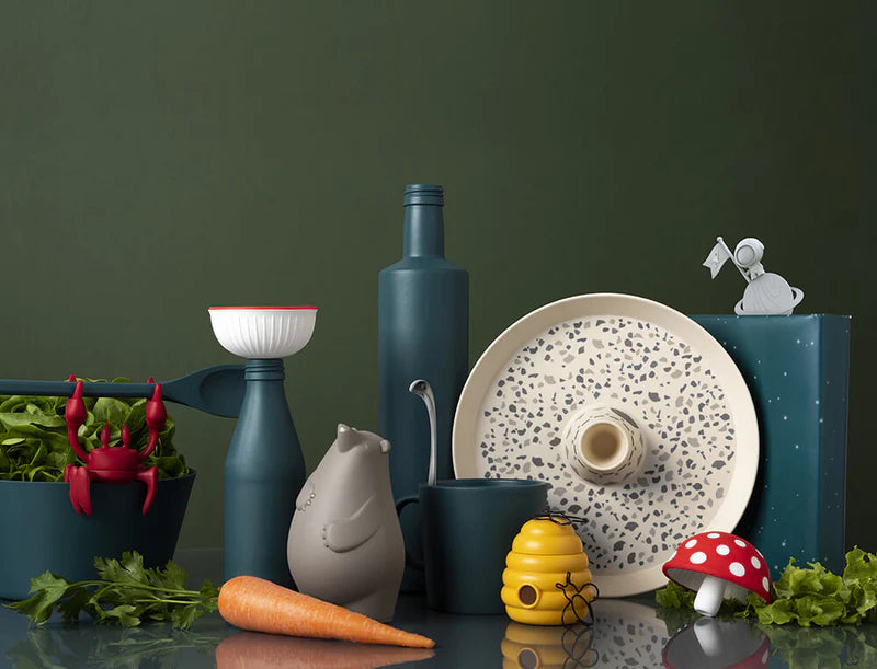 Assorted kitchen items and toys, including a carrot, honey pot, and mushroom, against a dark green background.