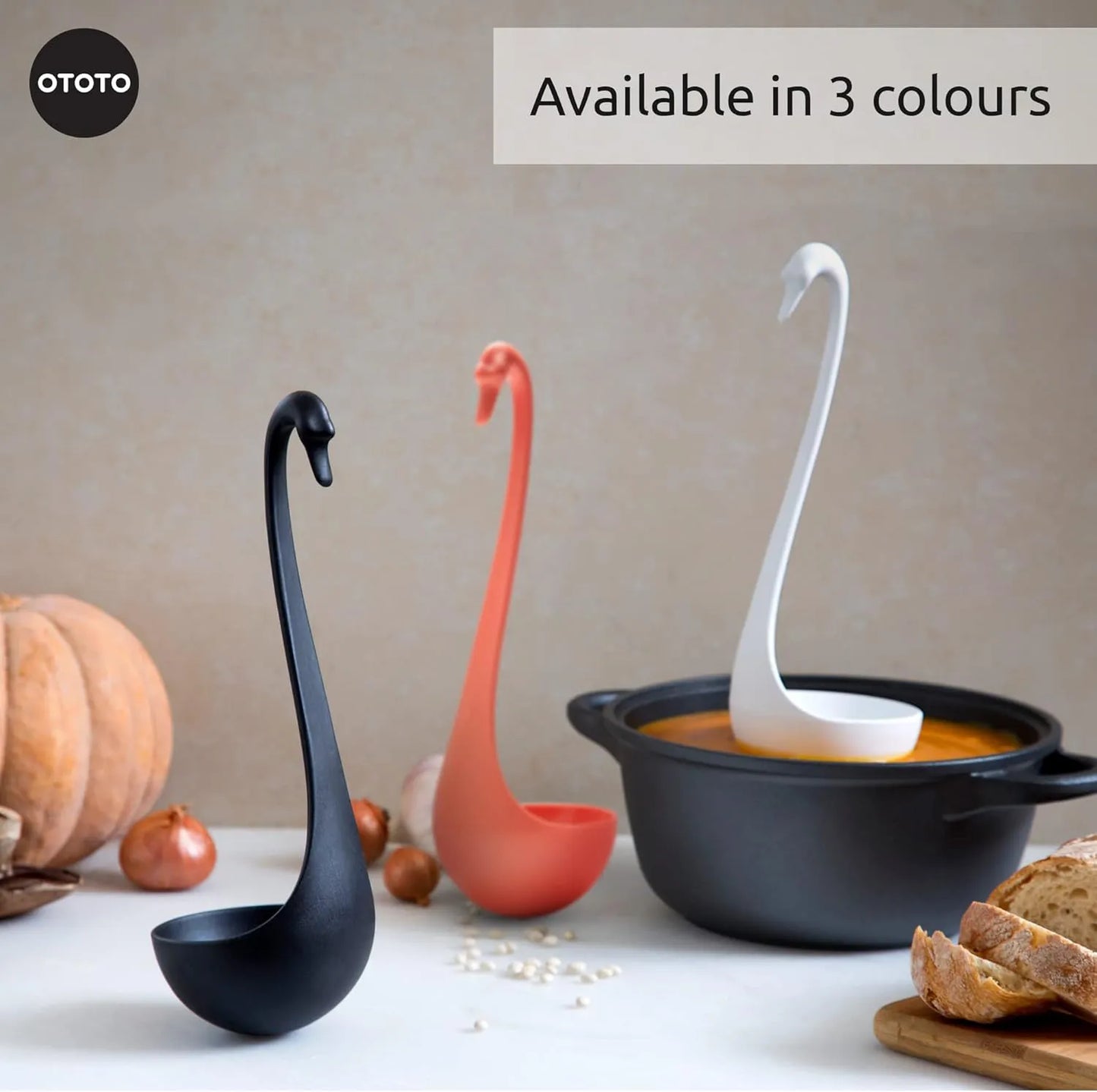Three Swanky swan-shaped ladles in black, coral, and white rest by a soup pot and bread.