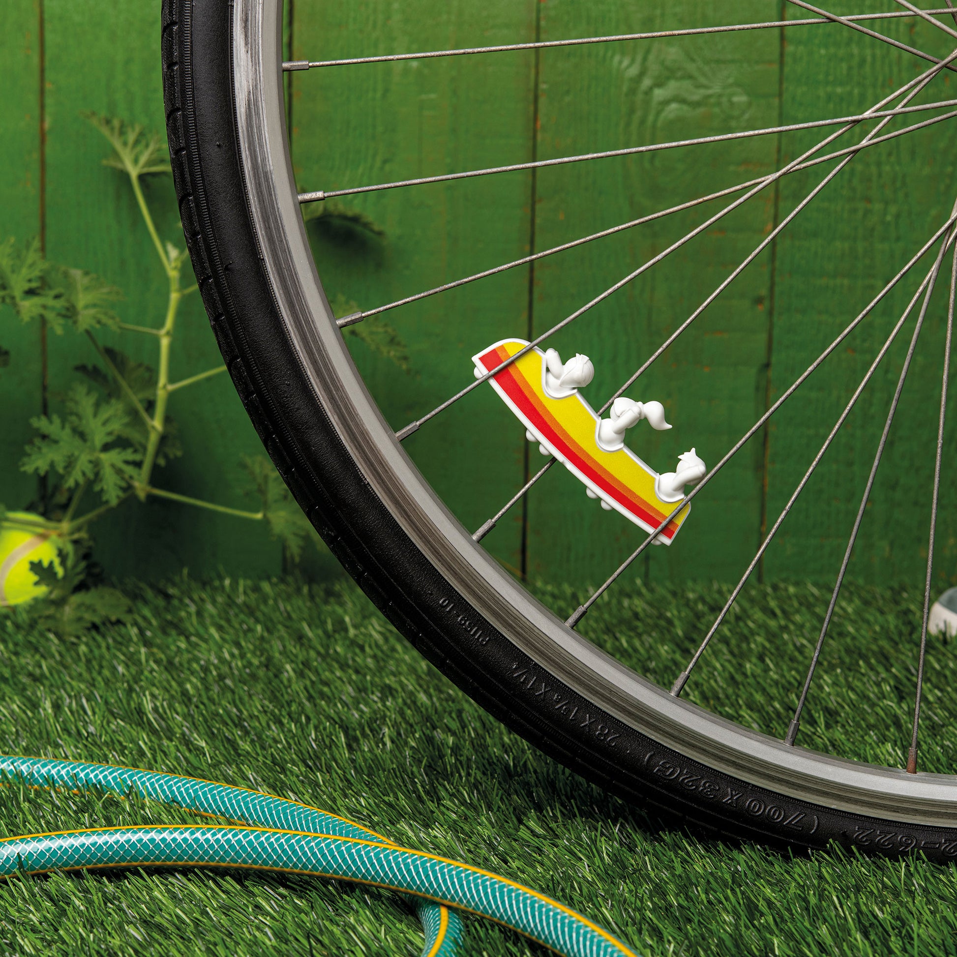 Close-up of a Rollerama accessory on bicycle spokes, resting on grass near a hose.