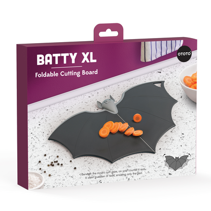 Batty bat-shaped folding chopping board by OTOTO in a purple-white box, pictured with carrots.
