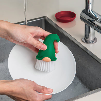 A person washes a plate with the OTOTO Beardy gnome dish brush by the kitchen sink.