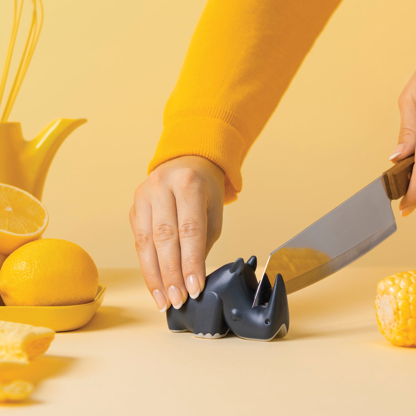 Someone slices a blue Blade rhino-shaped object with a knife among yellow fruit in the kitchen.