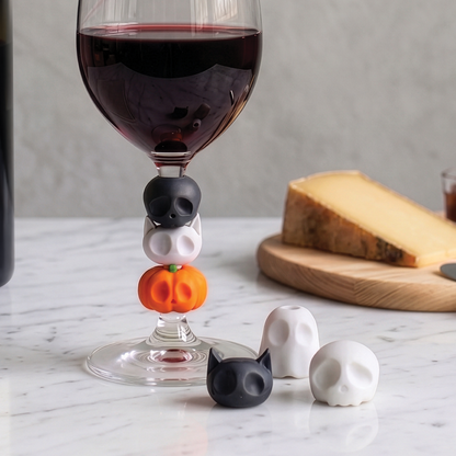 A "Boo Team" wine glass with Halloween charms, cheese board, and wine charms on a marble table.