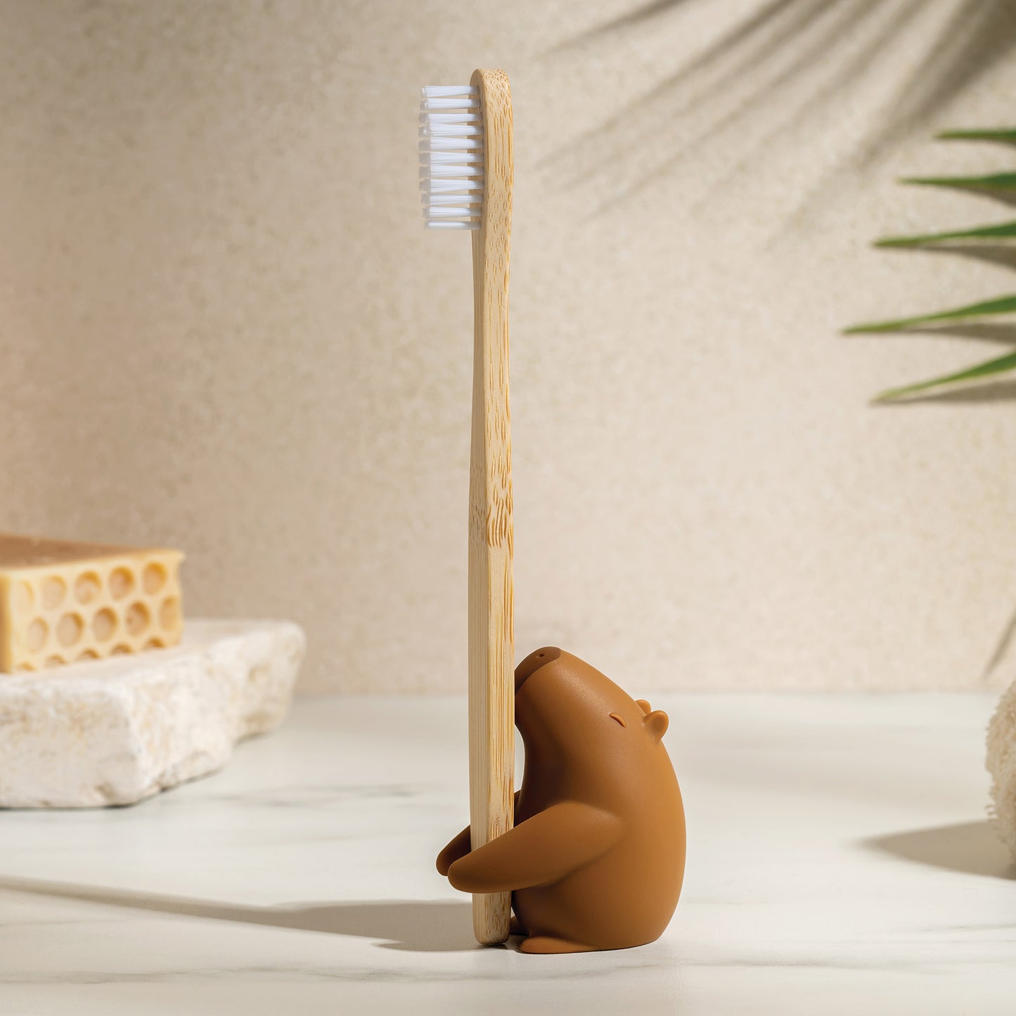 The Capybrush brown capybara holds a bamboo toothbrush on the bathroom counter.