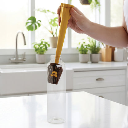 A hand uses the Cleo bottle cleaner to wash a bottle in a bright kitchen with plants.