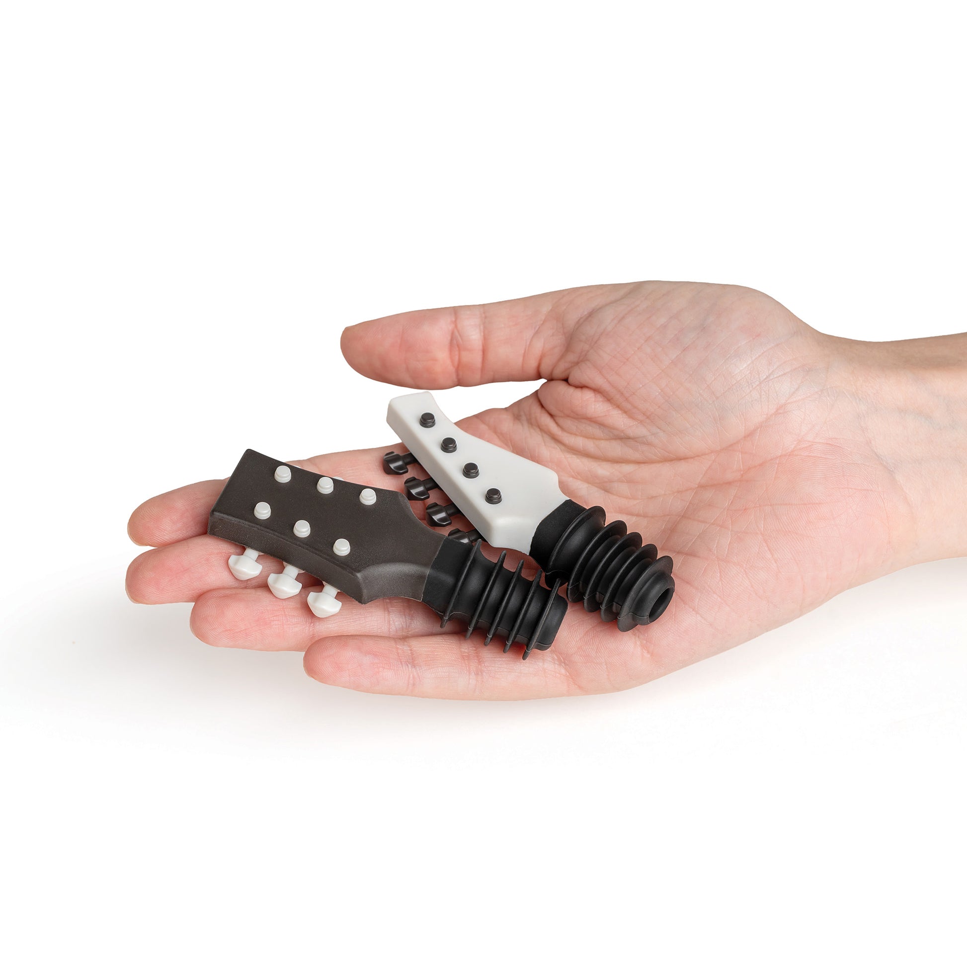 A hand holds two Cork N' Roll guitar headstock wine stoppers, one black and one white.