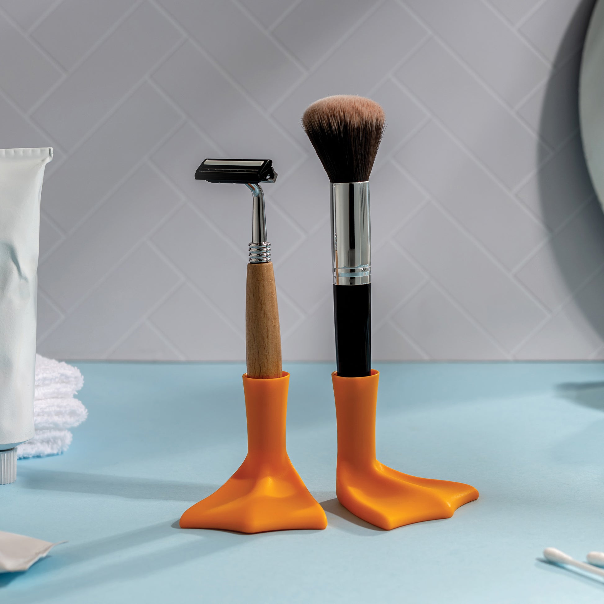 A razor and a Duck-Clean sit upright in orange holders on a blue surface.