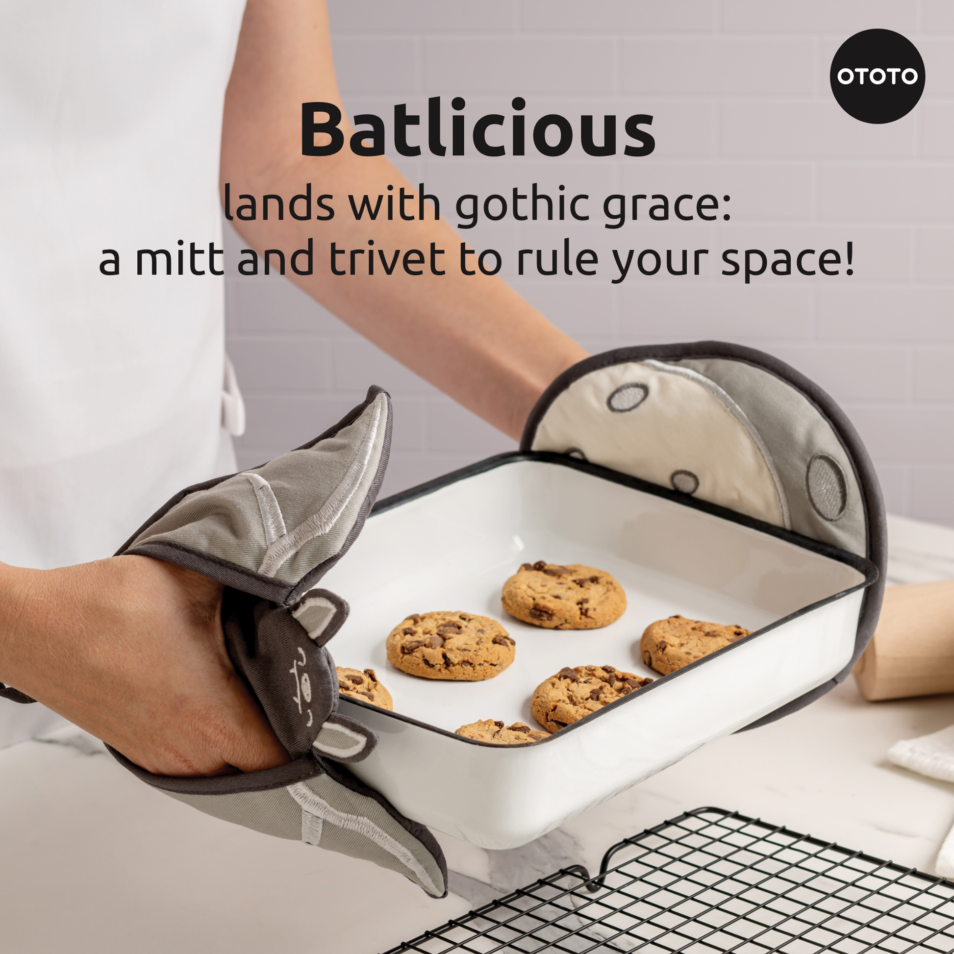 Someone uses Batlicious oven mitts to hold a baking dish full of chocolate chip cookies.