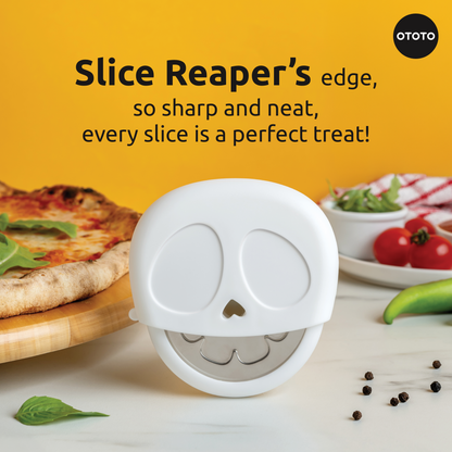 The Slice Reaper pizza cutter by OTOTO rests on a table with pizza, veggies, and spices nearby.