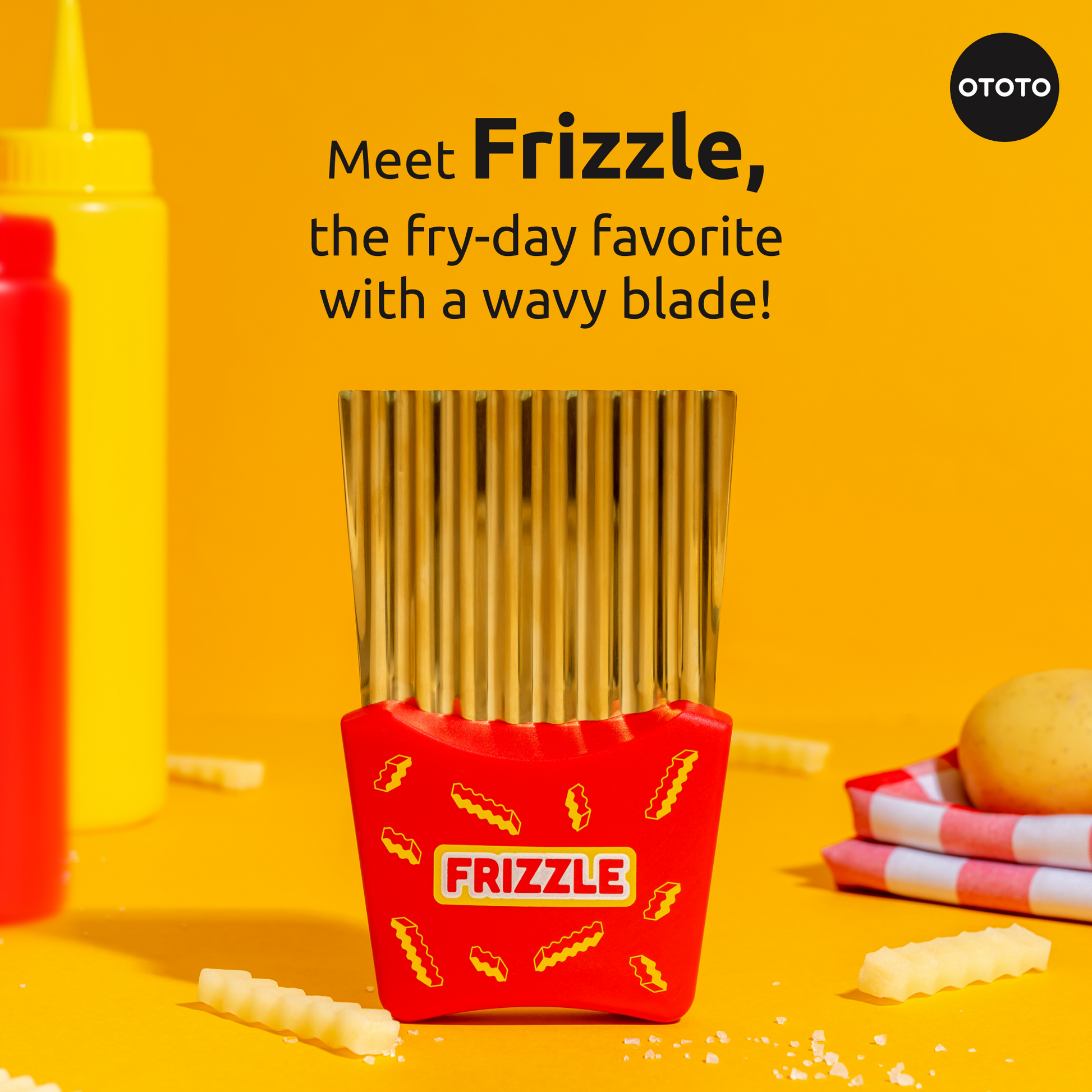 Frizzle, a crinkle fry cutter by OTOTO, stands on yellow beside fries, ketchup, and mustard.
