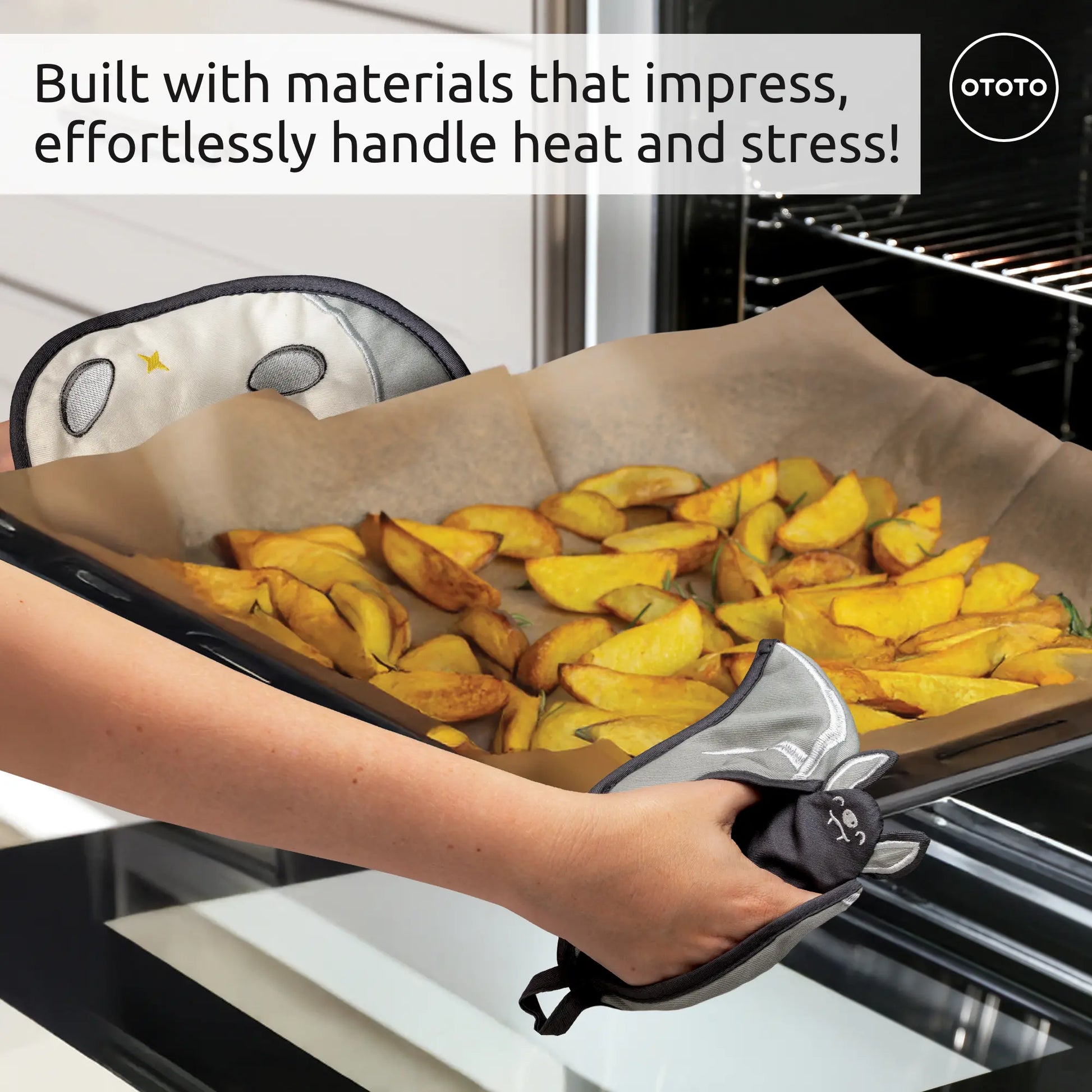 Hands with cute, gray Batlicious oven mitts remove a tray of potato wedges from the oven.