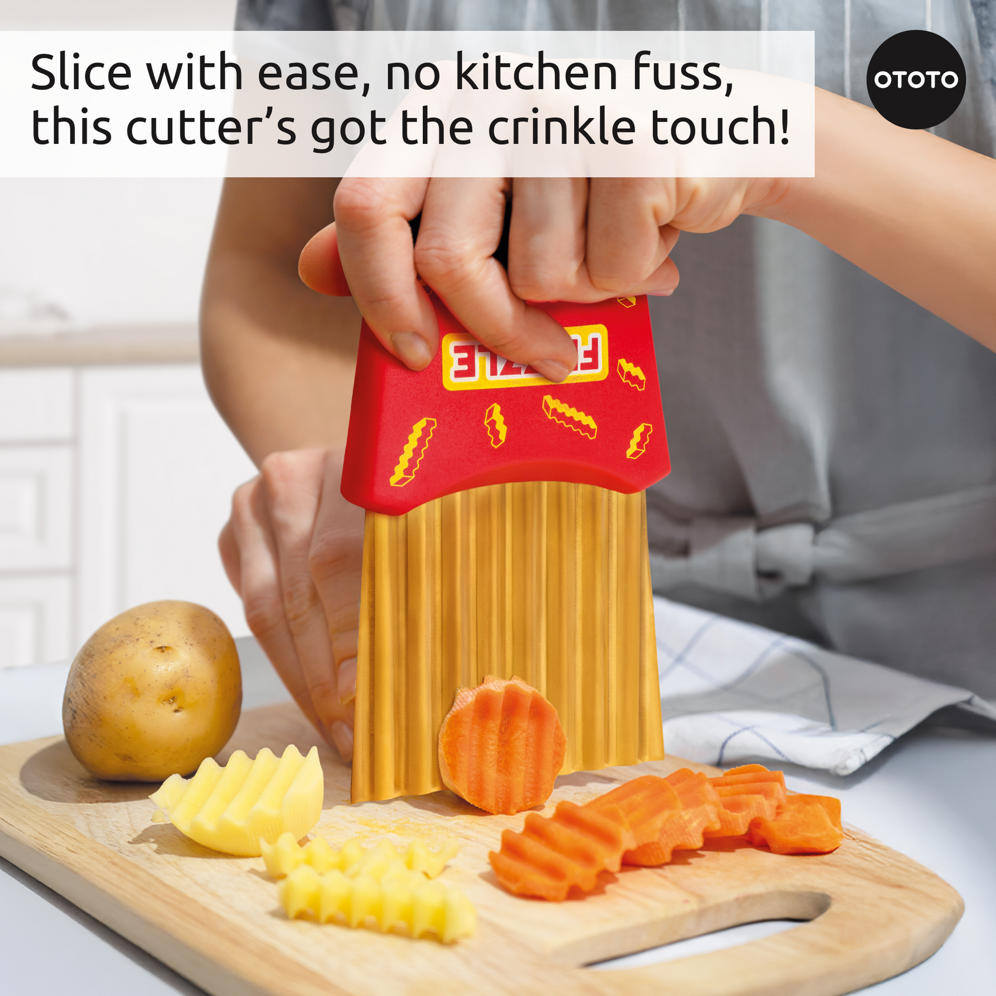 A person uses the Frizzle crinkle fry cutter to slice carrots and potatoes on a wooden cutting board.