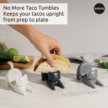 A hand places a taco in a black OTOTO Catos taco holder next to two other Catos holders.